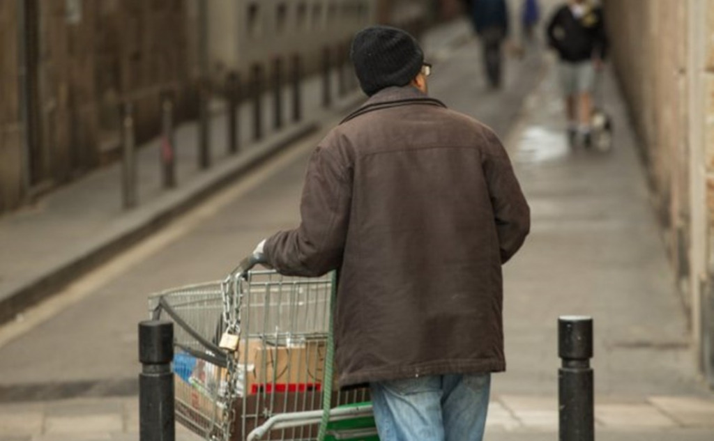 Un senyor d'esquena empeny un carret de supermercat pels carrers